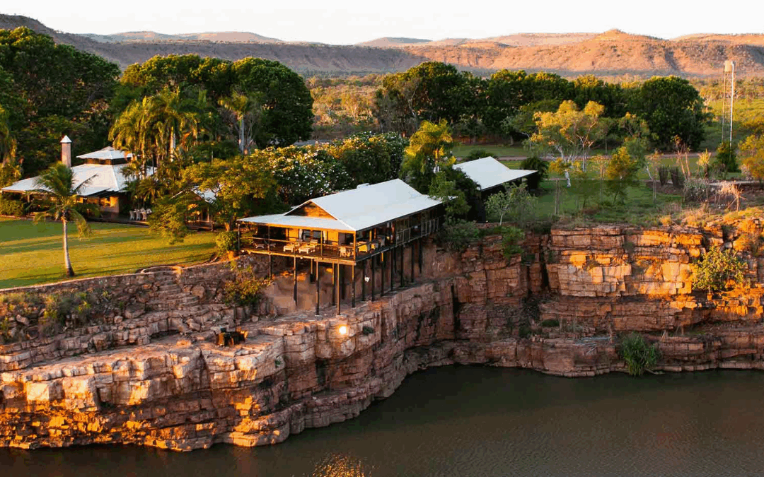 Luxury lodge perched on a rugged cliffside in El Questro, Western Australia, overlooking a serene river at sunset.