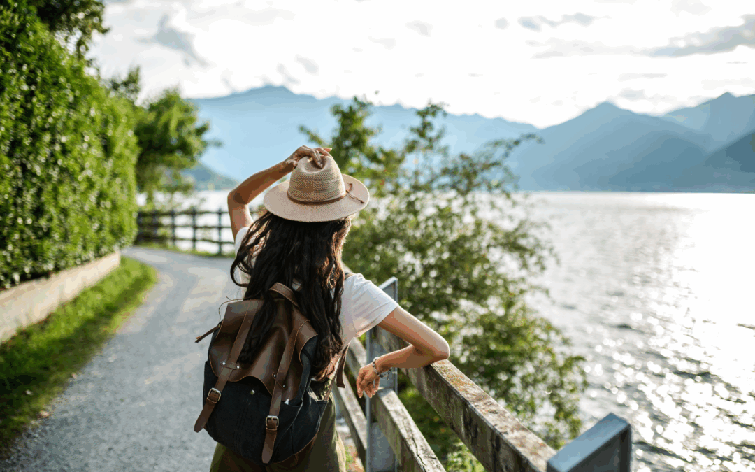Solo female traveller walking along a scenic lakeside path with a backpack and hat, symbolising independence and exploration